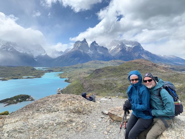 Two hikers in Patagonia sit on a rock with a lake and the Torres del Paine peaks in the backdrop.