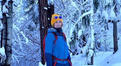 A woman standing on a trail among pine trees on a misty day.